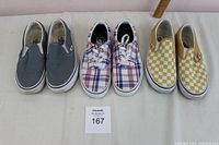 Top view showing three pairs of Vans shoes: gray slip-ons, red-white-blue plaid lace-ups, and yellow-white checkerboard slip-ons.