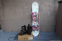 Snowboard standing upright with pink and white bindings, brown boots in front on box
