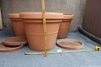 Three large terracotta planter pots with three matching saucers placed on a gray carpet, with a measuring stick showing height about 24.5 inches and a tape measure showing diameter about 29 inches.