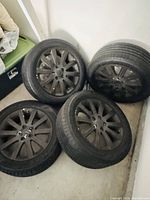 Four tire and rim assemblies leaning against a wall, front and side views visible