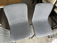 Two grey fabric upholstered dining chairs with black legs, one with a visible small dark stain on the seat surface.