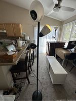 Two black metal floor lamps with adjustable heads and round bases in a living room setting, showing size and condition.