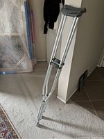 Standing single aluminum walking crutch showing adjustable height and gray underarm pad.