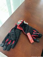 Pair of black and red Grease Monkey gloves laid on wooden surface, showing their design and material.