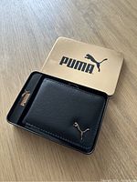 Photo of the closed black Puma billfold wallet inside the original gold metal Puma box.