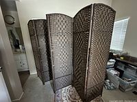 Full view of six-panel brown woven privacy divider standing on carpeted floor in a room.