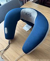 Full view of the U-shaped heated neck massager pillow showing navy blue fabric with grey interior and connected power cord.