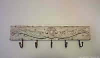 Full front view of the rustic style wooden wall hanger mounted on a white wall showing the decorative carved top and five rusted metal hooks.