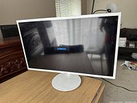 Front view of the Samsung white framed LED monitor on a wooden table, with the screen off showing no scratches or dents.