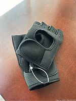 Pair of new black fingerless fitness gloves folded and stacked on a table, with visible tag and no signs of wear.