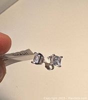 Close-up of two silver stud earrings showing the clear CZ stones and attached tag with brand information.