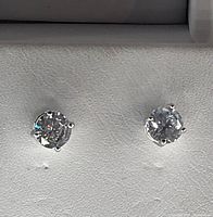 Close-up front view of silver stud earrings with circular clear stones in prong setting on gray background