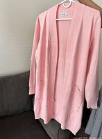 Front view of pink open-top sweater with two front pockets and ribbed detailing, displayed on hanger.
