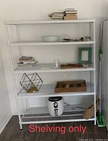 White metal shelving unit assembled and partially loaded with items including books, decorative objects, and kitchen items.