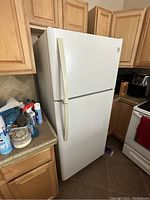 White Kenmore refrigerator in kitchen corner next to wooden cabinetry and other kitchen appliances.