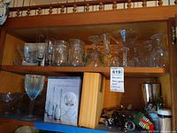 Shelf with assorted clear glassware, Paul Revere boxed vodka glass set, bottle openers, and bar accessories