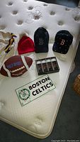 View of three hats (two Boston Red Sox caps and one red knit hat), Polo Sport football, Boston Celtics plate, and golf ball boxes