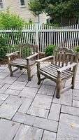 Two weathered teak benches on stone patio below white picket fence