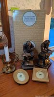 Metal base electric candle light, brass Studious Monkey bookends, two small photo frames on a wooden surface with a box labeled 'Brass Studious Monkey Bookends' in background.