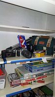 Shelf holding cameras, lenses, tripod, Canon camera cases, photographic film, and accessories.