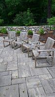 Five chairs arranged on stone patio in front of low stone wall and landscaping.