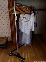 Metal clothing rack with wooden hangers and clothing items, showing the rack's mobility and multiple hangers.