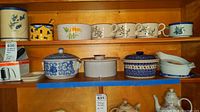 Shelved stoneware dishes with floral designs and several lidded casseroles in blue, beige, and polka dot patterns plus stoneware mugs and ceramic containers