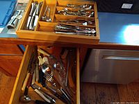Wooden flatware tray with spoons, forks, knives, butter knives, and variety of metal kitchen utensils in drawer below