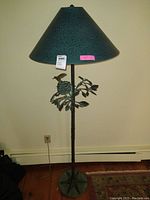 Full view of floor lamp showing the lamp shade, the bird on nest with leaves metal design on the pole, and round base