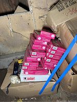 Stack of multiple unopened Pinnacle Ribbon golf ball boxes with pink packaging. Polaroid i-Zone camera and golf tees at base.