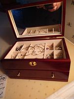 Open wooden jewelry box showing compartments filled with assorted costume jewelry including rings, earrings, pins, and necklaces.