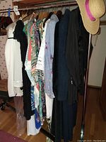 Wide view of clothing rack holding assorted women's garments on wooden hangers with a straw hat on one end