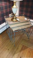 Front angled view of set of three nesting tables with metal frames and wicker tops, stacked and pictured with a lamp on top.