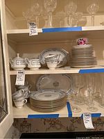Two shelves of Oxford Bone China plates, cups, saucers, sugar bowl, serving platters, and glassware above the china.