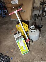 Photo shows propane tank, Sprayway glass cleaner box, Stanley high pressure washer box, and long handle garden tool on garage floor.