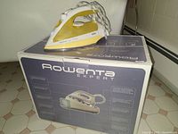 Braun Easy Style iron placed on top of a boxed Rowenta Expert steam generator iron on tiled floor.