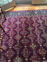 Close-up showing the red diamond lattice pattern with floral motifs and a corner of wooden chair leg.