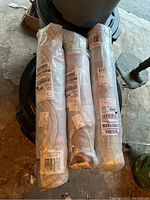 Three rolled area rugs wrapped in plastic packaging with shipping and barcode labels visible, placed on a trash can lid.