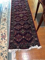 Full view of burgundy runner showing pattern, fringe, and scale against hardwood floor
