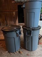 Three Rubbermaid Brute trash bins stacked and standing, showing general condition and lids.