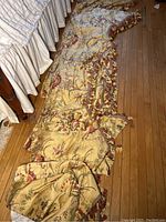 Five floral design fabric valances laid out on wooden floor, showing full length and tassel trim.