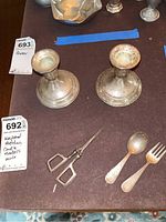 Top view of sterling silver weighted candle holders with pair of vintage scissors, a fork and spoon on a brown surface all tagged.