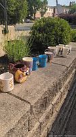 All twelve mugs lined up outdoors on stone ledge showing varied themes and styles including character mugs and graphic prints.