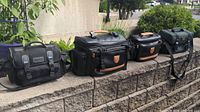 Photo showing four black camera bags arranged on a brick ledge outdoors, highlighting their size and general condition.