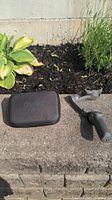 Photo of DJI Osmo gimbal next to the black carrying case on a concrete surface with mulch and plants in the background.
