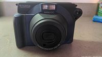 Front view of the Fujifilm Instax 100 camera showing the lens, flash, and grip.