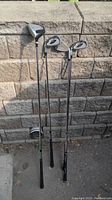 Four left handed golf clubs standing upright against a retaining wall. Includes driver and irons with graphite shafts and black grips.