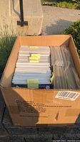Box filled with many bagged and boarded comic books arranged vertically, some with yellow sticky notes on top.