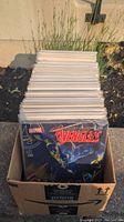 Box filled with comic books, front visible Avengers #2 comic, shows Marvel branding and a superhero figure.