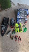 Lot of mixed toys on concrete floor including two boxed Black Ghost micro indoor RC helicopters, two toy boats, and various action figures